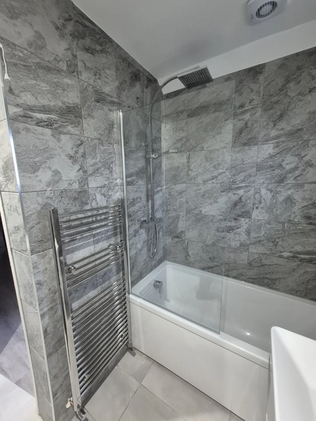 Bath with glass shower screen and chrome heated towel rail — Queenborough bathroom renovation